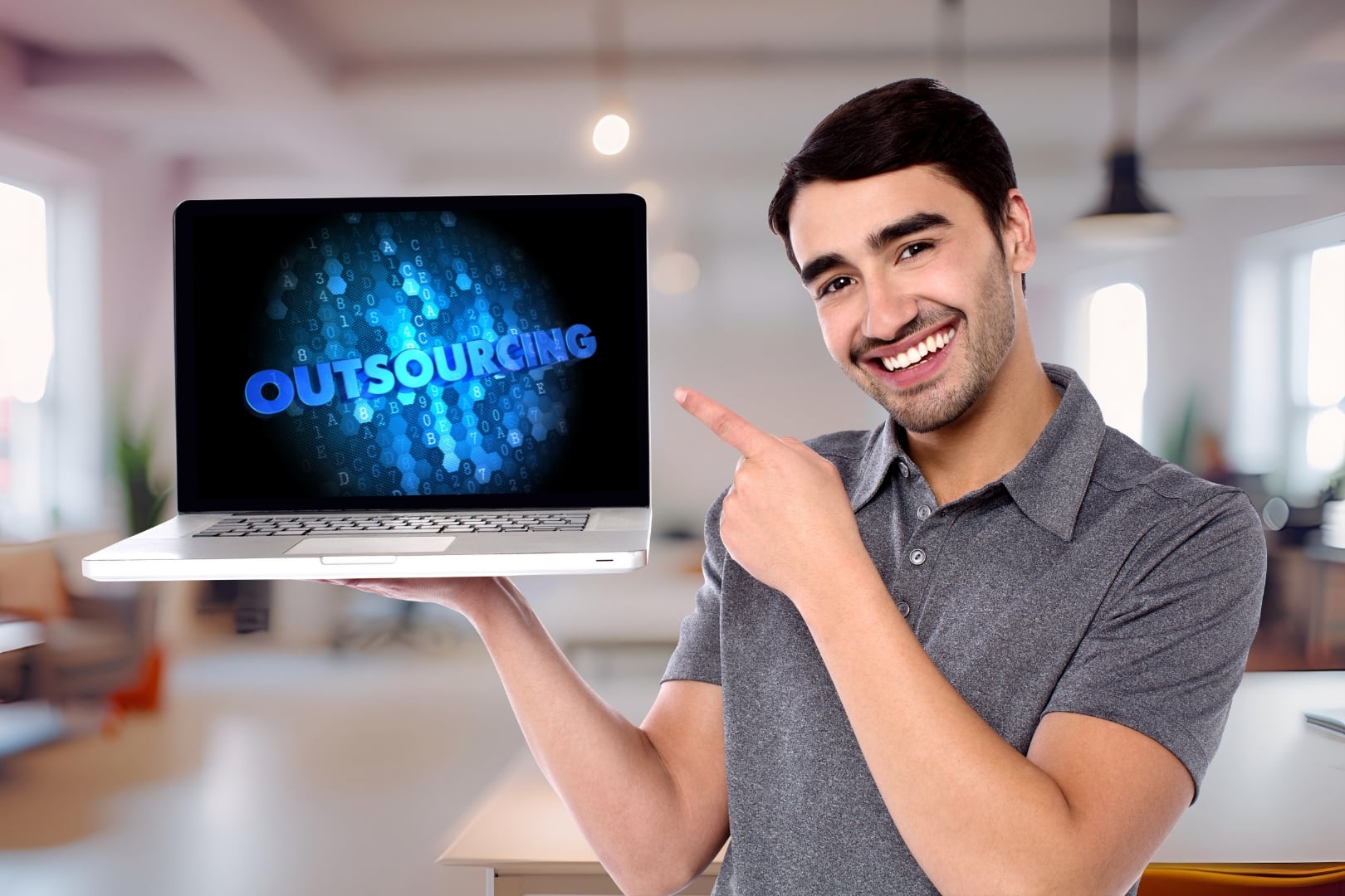 Lächelnder Mann zeigt auf einen Laptop mit dem Schriftzug ‚Outsourcing‘ im Büro