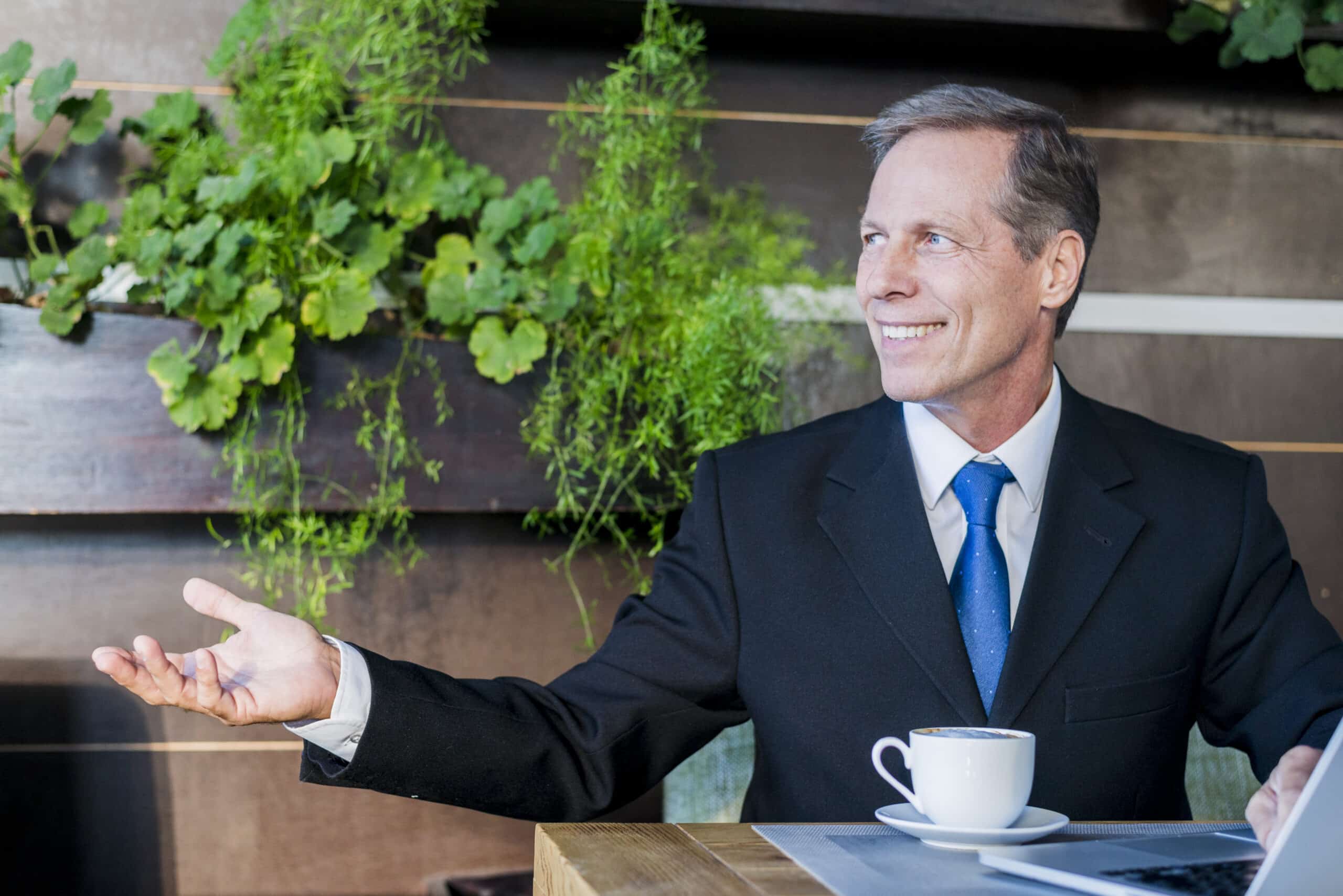 Person im Anzug sitzt mit einer Kaffeetasse und gestikuliert