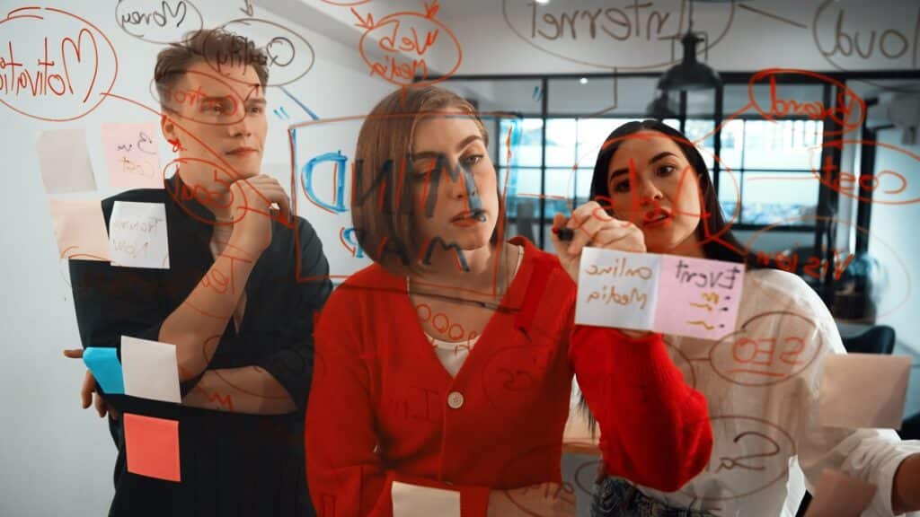 Drei Personen erstellen Notizen und Skizzen auf einem Glasboard