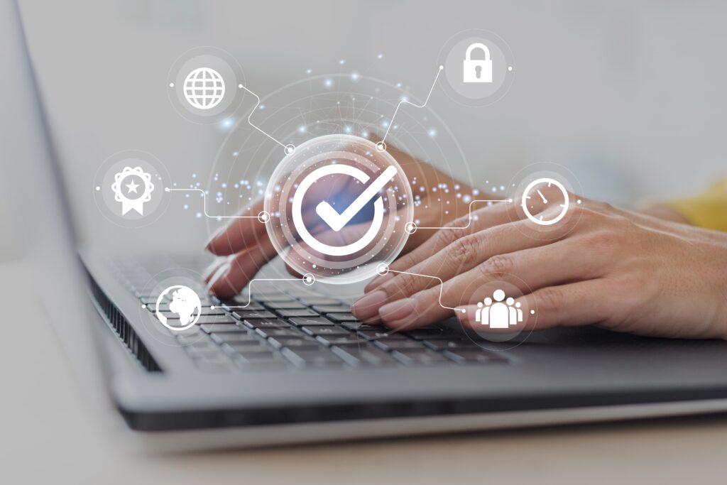 Hände tippen auf einem Laptop, darüber schweben digitale Sicherheitssymbole