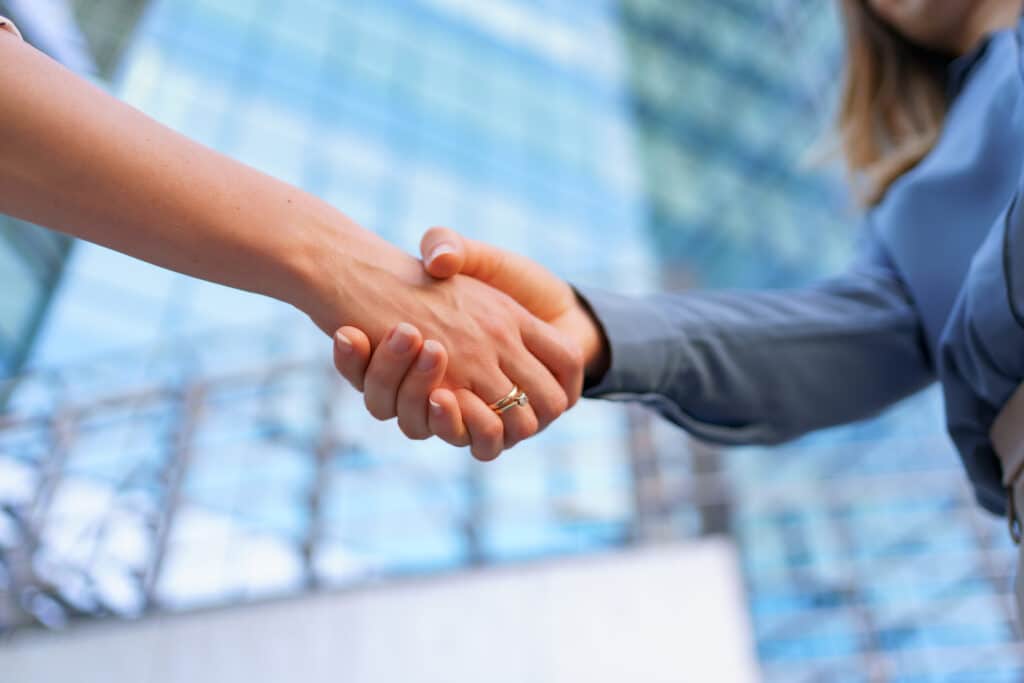 Zwei Personen geben sich vor einem Bürogebäude die Hand