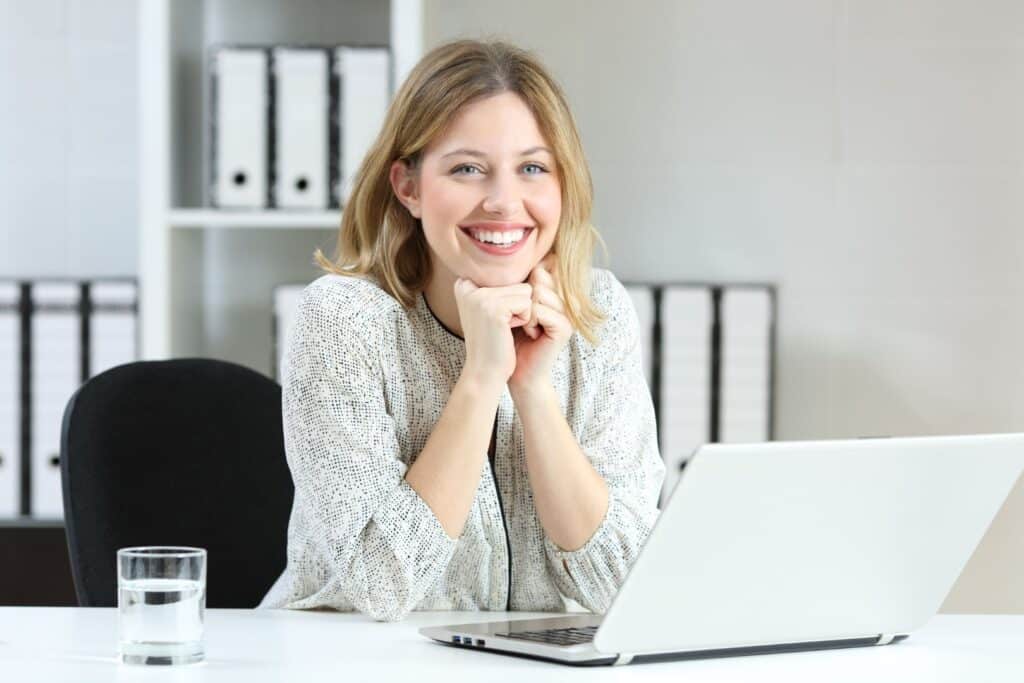 Lächelnde Frau sitzt an einem Schreibtisch und arbeitet am Laptop