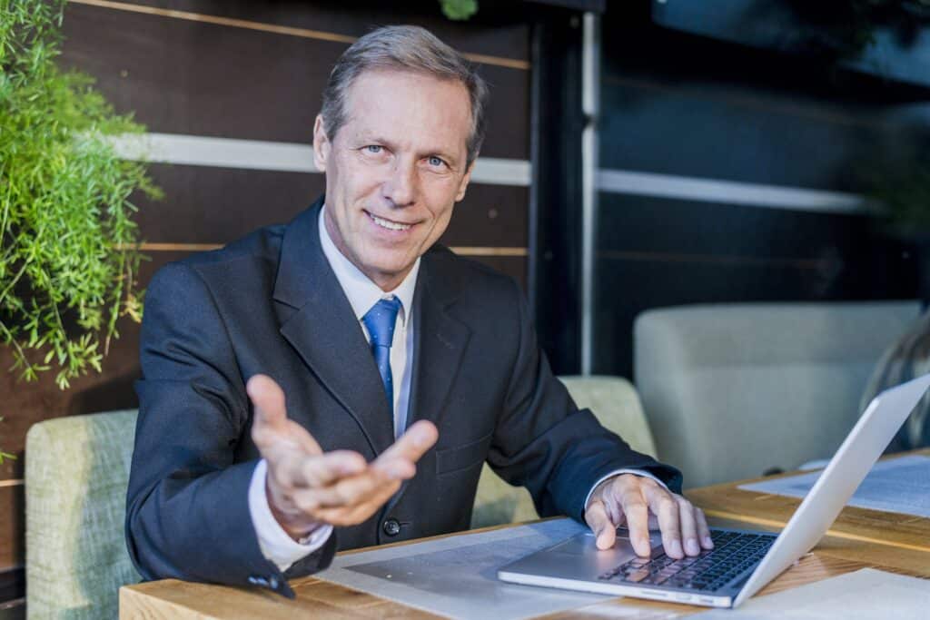 Geschäftsmann im Anzug arbeitet an einem Laptop und gestikuliert lächelnd