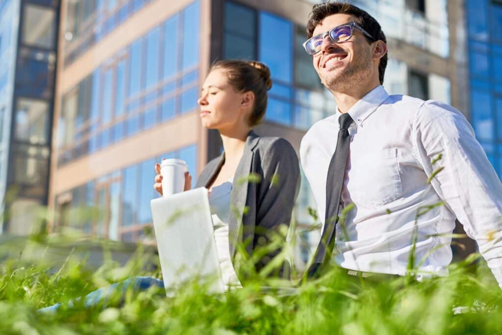 Nachhaltigkeit im Mittelstand: Zwei Mitarbeitende sitzen entspannt im Grünen vor einem Bürogebäude