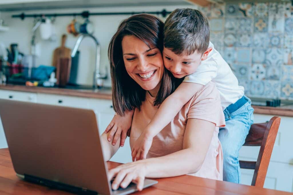 Mutter arbeitet im Homeoffice mit Kind, das sie umarmt